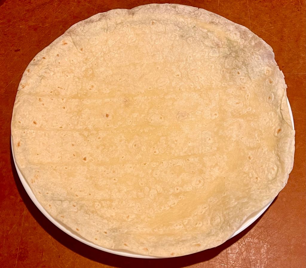 A steamed tortilla on a plate that has been heated and is ready for filling for bean burritos.