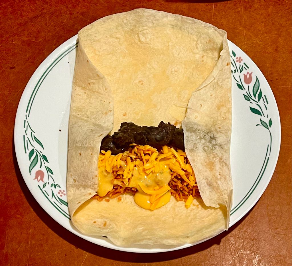 A tortilla on a plate with the side flaps folded over the filling for a bean burrito. 