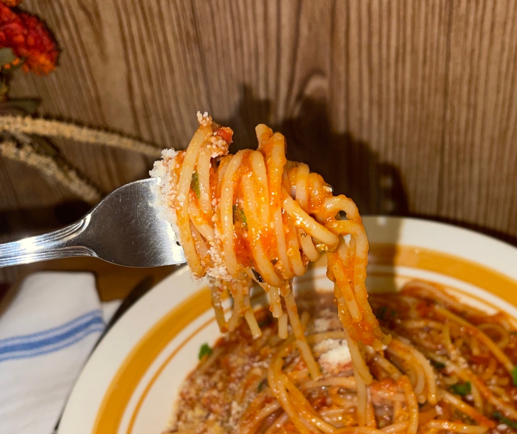 A photo showing cooked spaghetti twirled on a fork. The spaghetti has flecks of parmesan and a parsley garnish. 