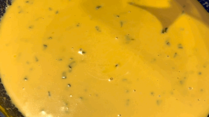 A GIF showcasing the nacho cheese sauce. A purple corn tortilla chip is scooping up the nacho cheese and holding it to the camera as some drips off.